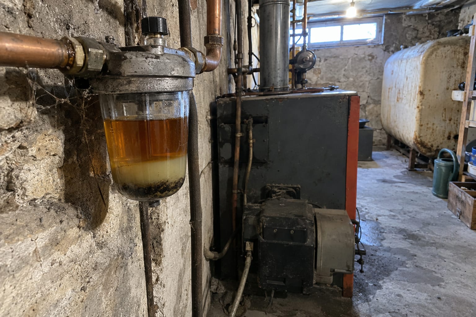 Un filtre à fioul à bol transparent, avec une couche d’eau trouble et un dépôt sombre au fond.